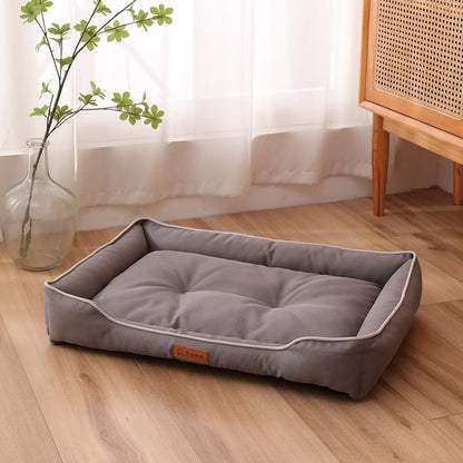 Gray pet bed on a wooden floor with a plant and cabinet in the background
